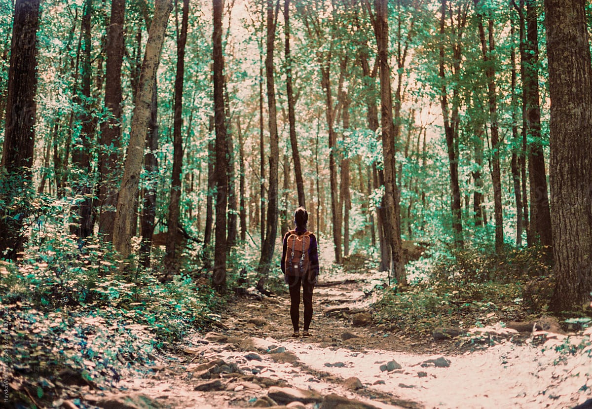 Girl standing in middle of trail in bright green forest standing with backpack