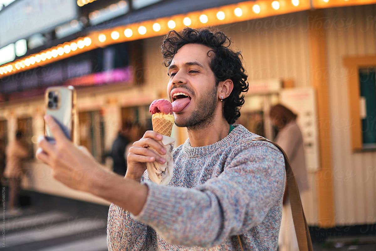 A young man using his mobile phone while enjoying an ice cream.