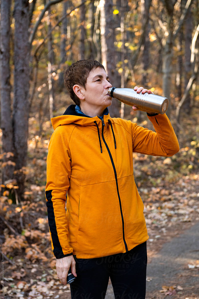 Middle-aged woman drinking water while walking/hiking in forest
