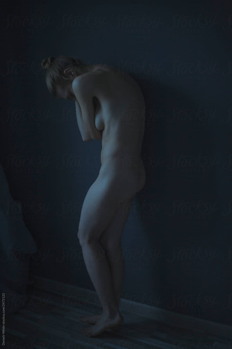 a girl is standing without clothes, covering herself on a dark background