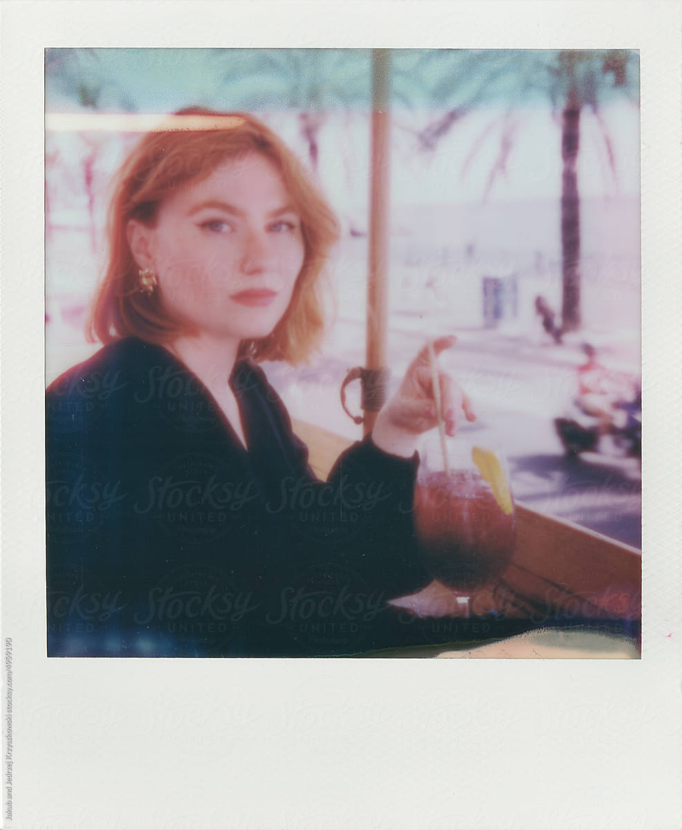 Polaroid of a woman looking at the camera and drinking a cocktail