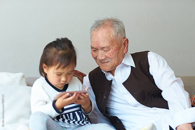 senior asian man watching his great granddaughter using smart phone