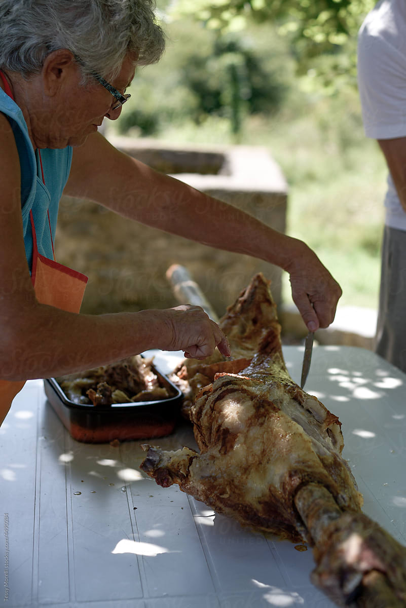 Elderly woman cutting the meat of a lamb after roasting