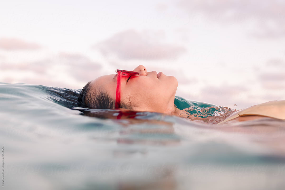 Woman with sunglasses floating in the sea at sunset