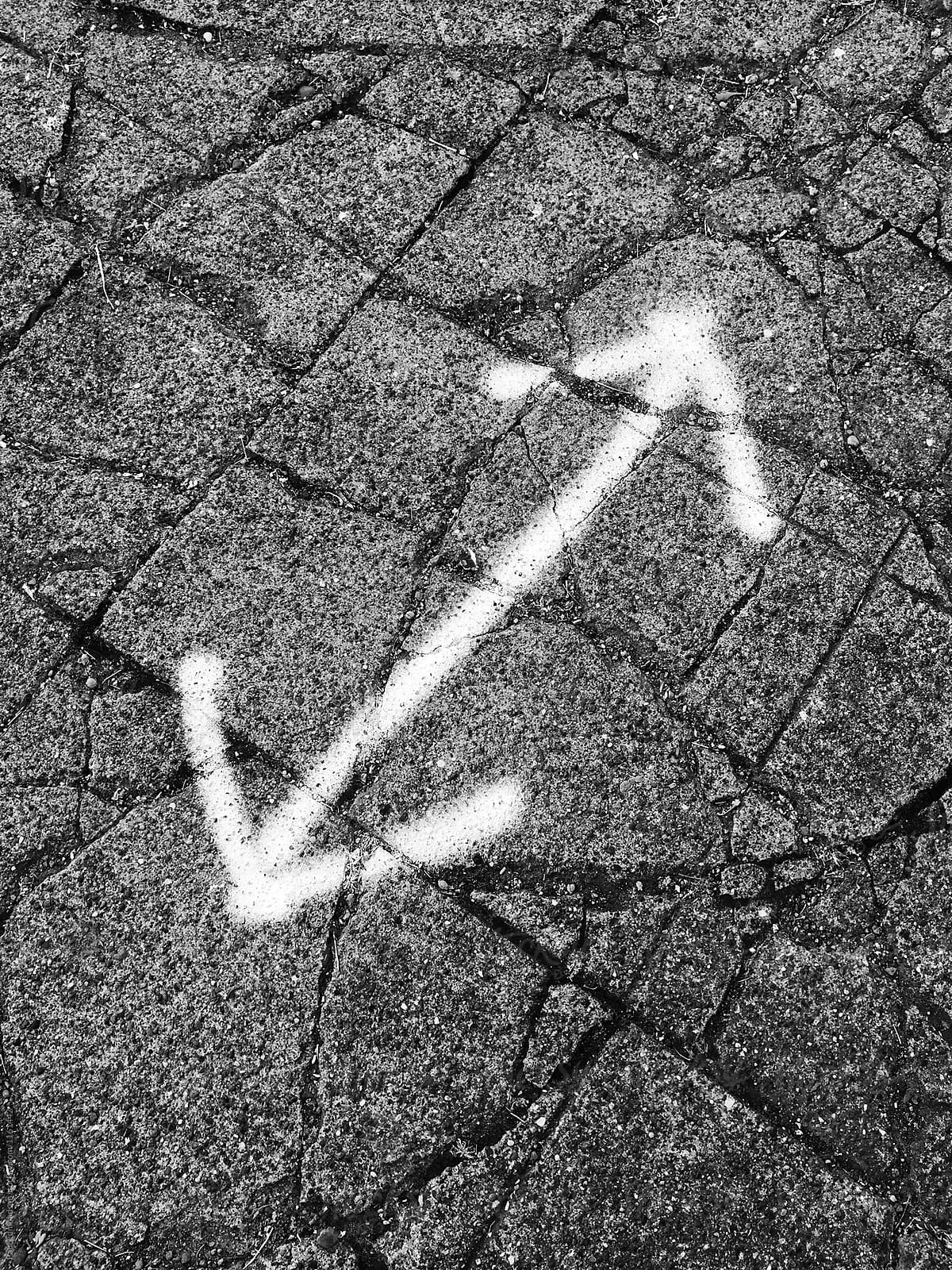 Spray painted double arrow sign on worn and cracked sidewalk