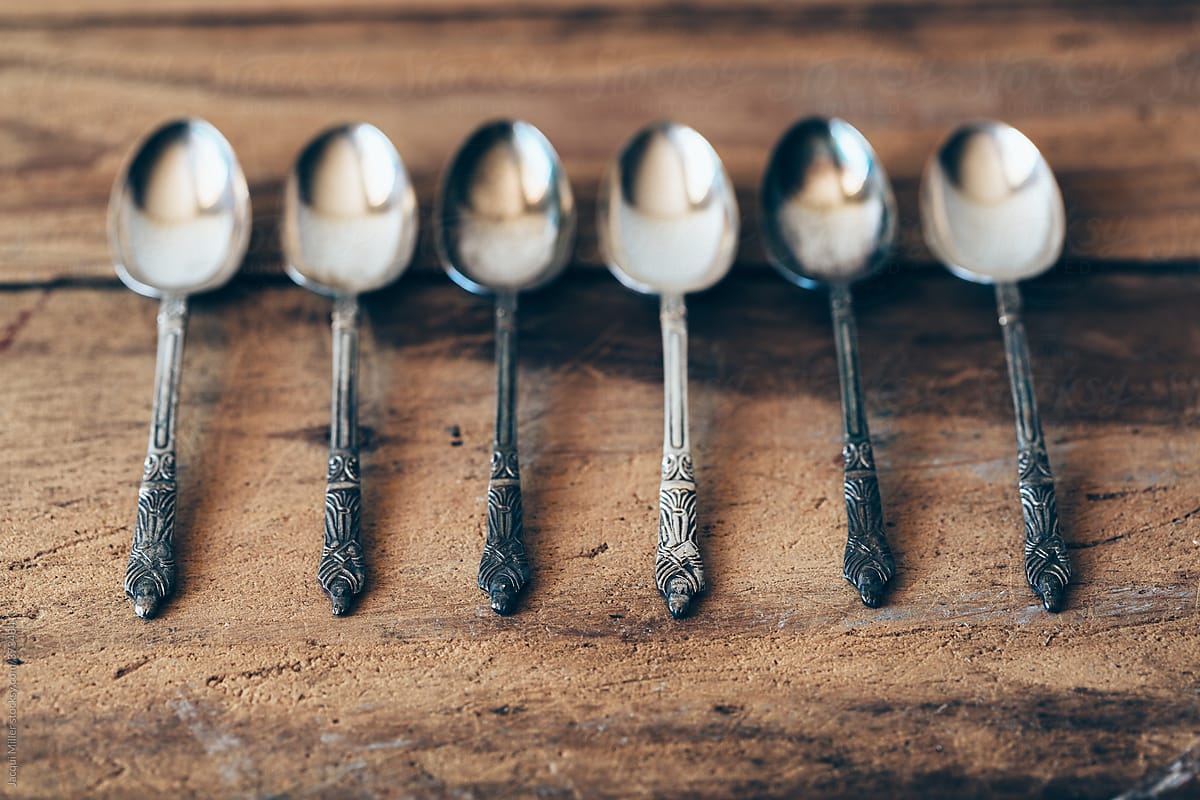 A row of six antique Apostle teaspoons on a rustic wooden table