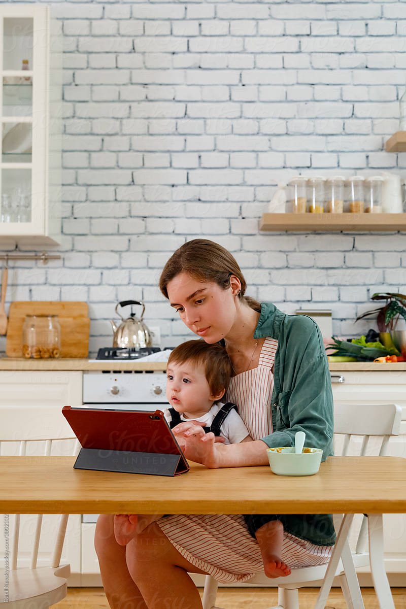 Positive mother and toddler son using tablet in kitchen