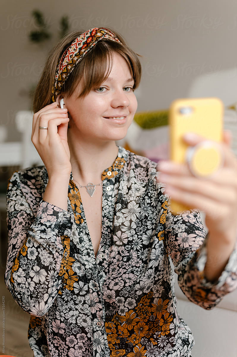 Cheerful woman with earphones using smartphone at home