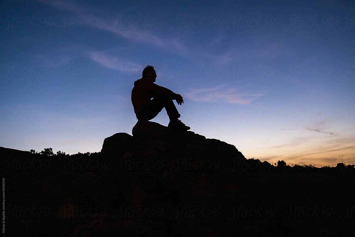man sits on rock during sunset