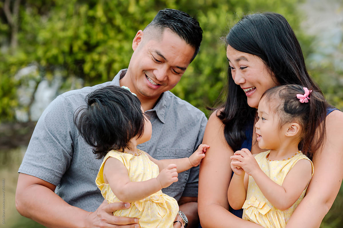 Smiling asian parents holding young daughters outdoors