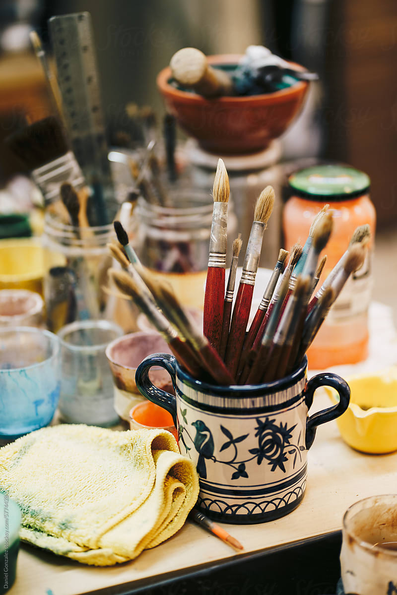 Paintbrushes placed in cup near cups of paint in on table