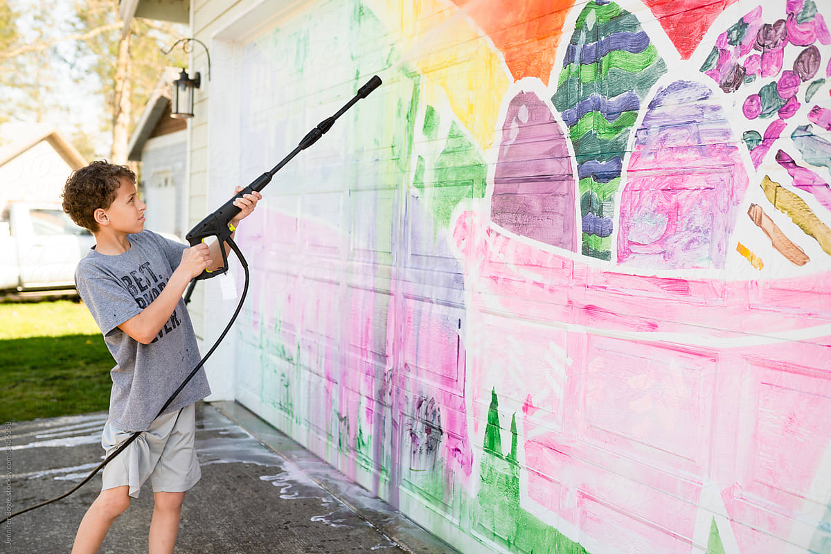 Boy cleans mural off garage door with power washer