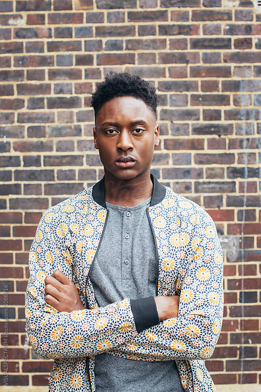 London Street Style - Outdoor Portrait of Good-Looking Young Black Man Standing in Front of Exposed Brick Wall