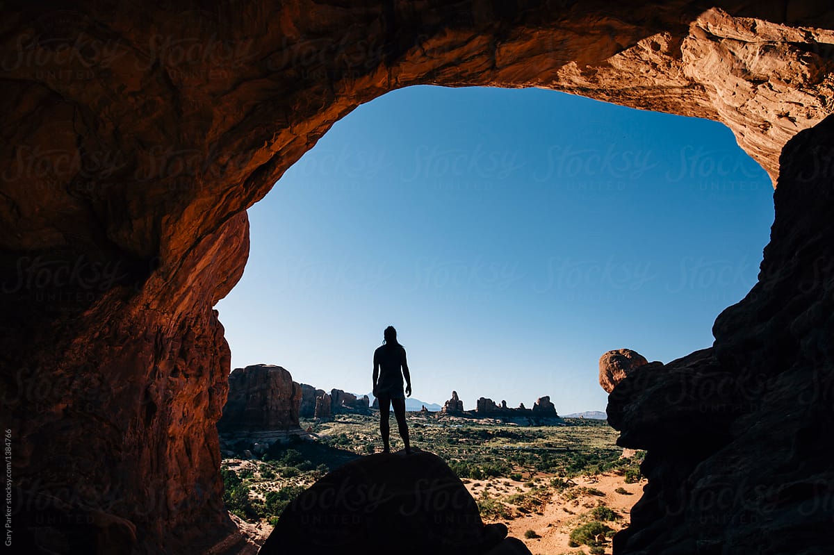 A woman standing under a large rock arch