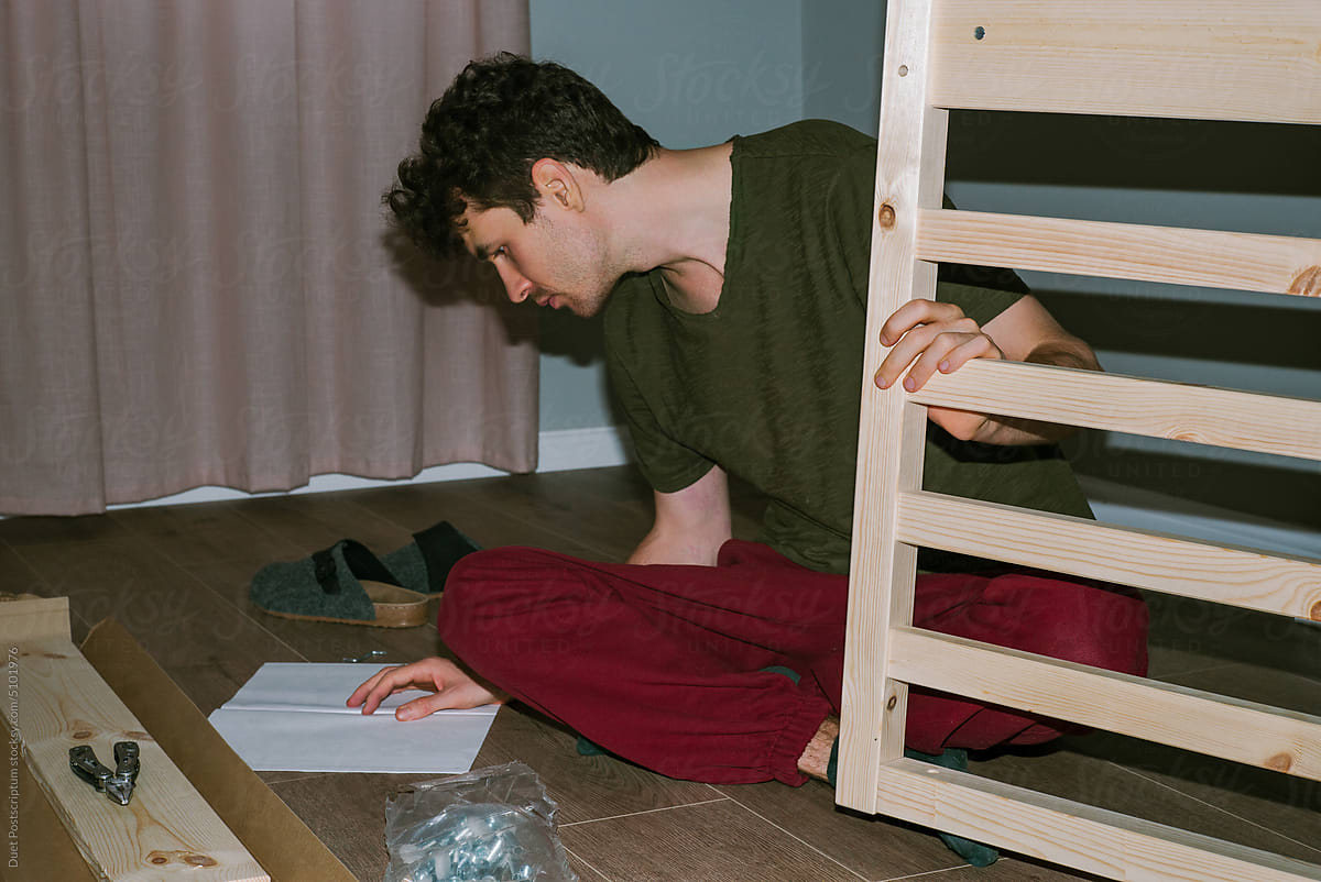 A curly-haired man studies the instructions for assembling a new bed
