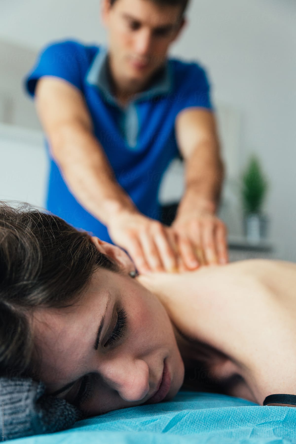 Close up of a beautiful young woman lying on a bed receiving a back massage by a young physiotherapist