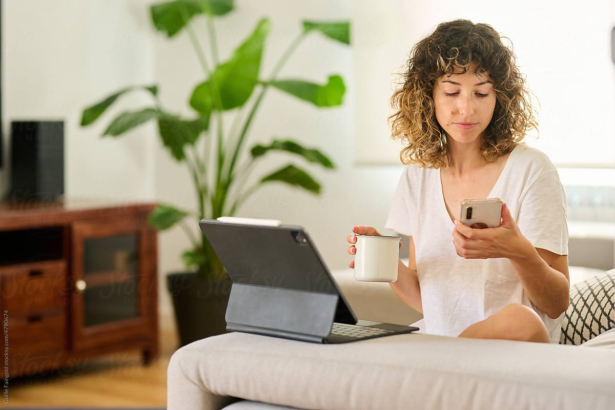 Woman holding cup of coffee and looking at mobile phone