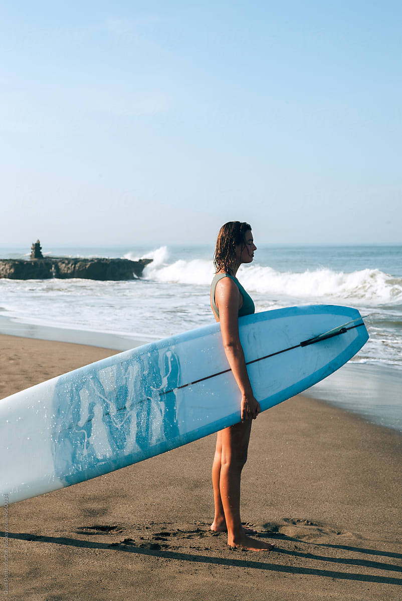Silhouette of a young woman with a long surfboard on the beach