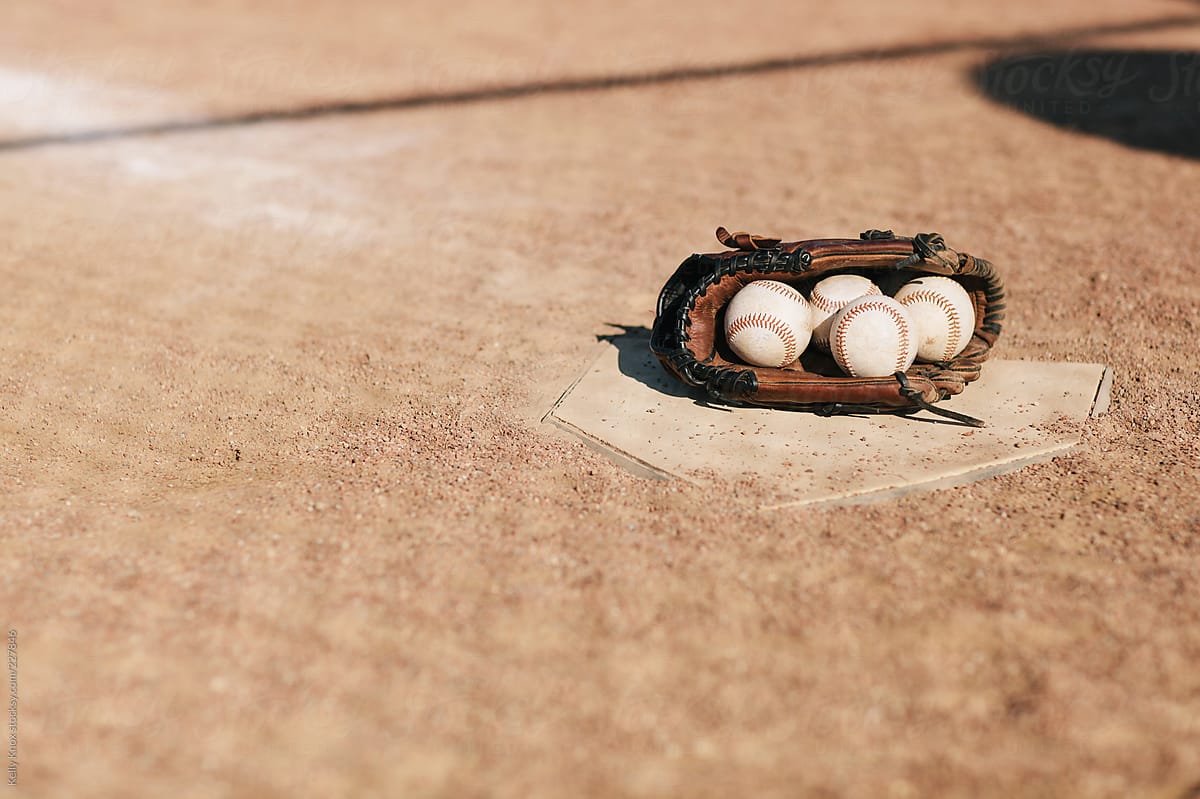 baseball glove full of baseballs rests on home plate