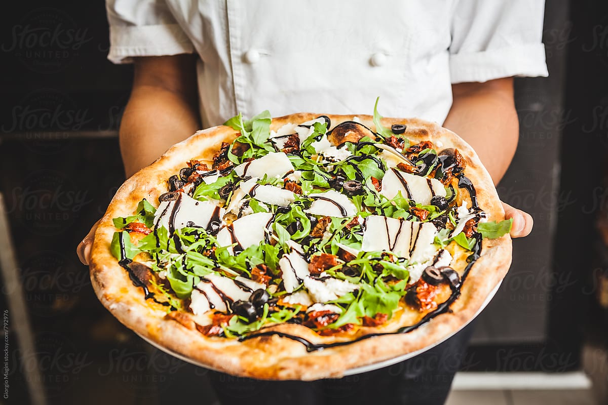 Showing a Freshly Baked Pizza with Rocket Salad, Black Olives, Parmesan Cheese and Balsamic Vinegar