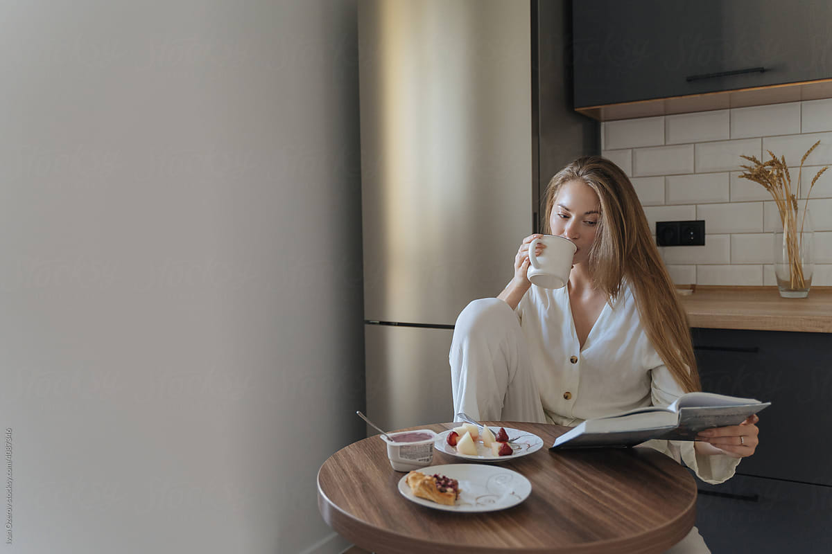 woman drinking coffee and reading a book in the kitchen
