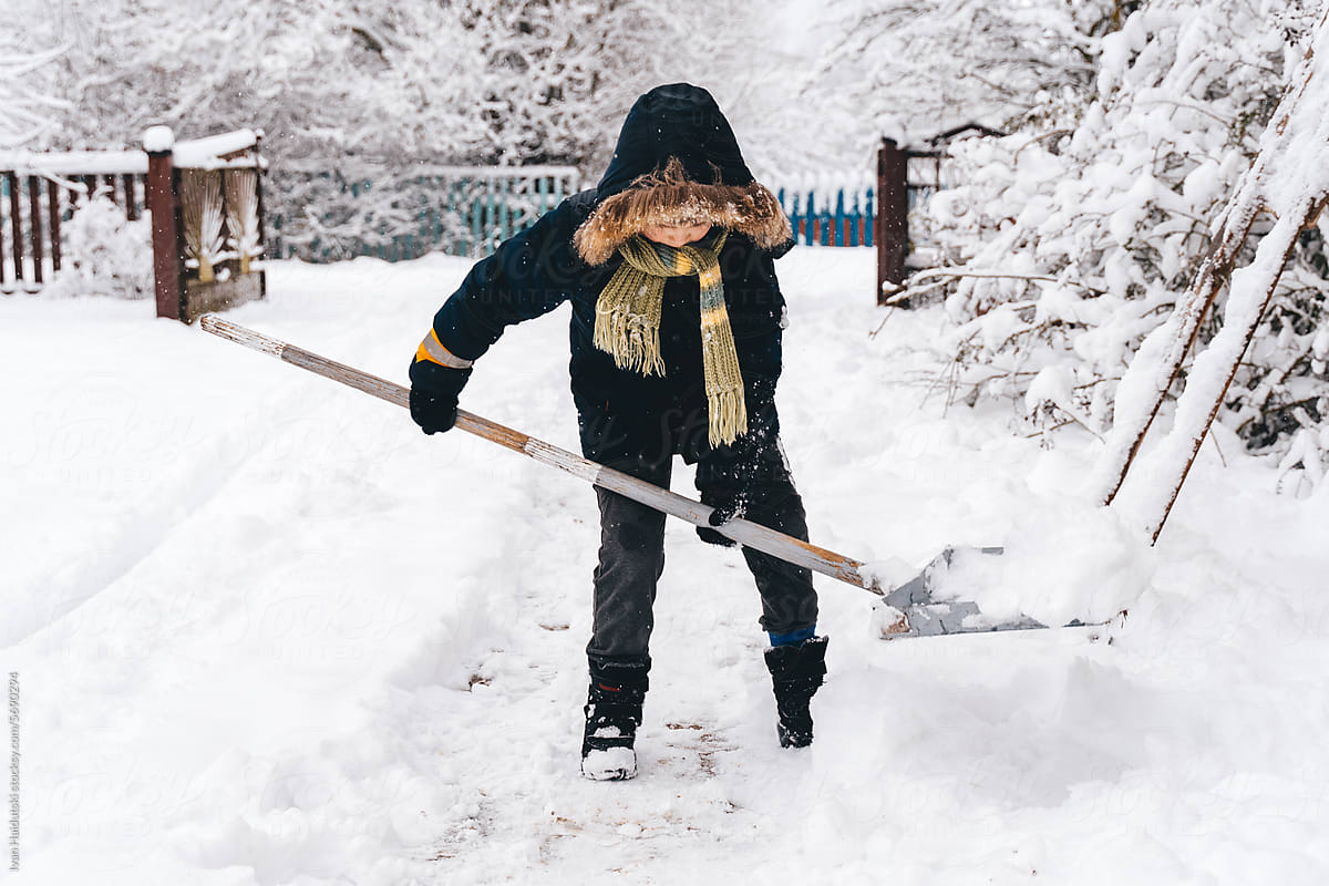 Kid Boy clearing snowy path in a suburban or countryside house yard