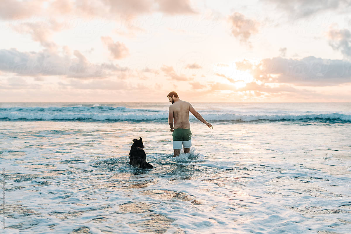 Man walking into ocean with dog