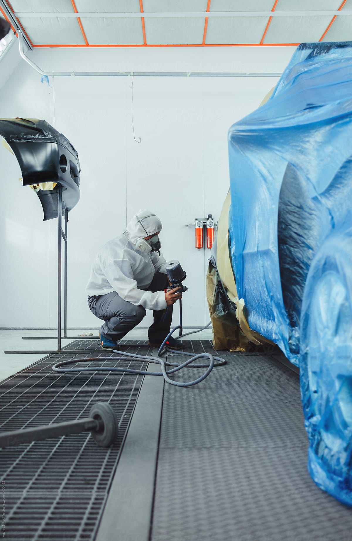 Worker/painter working on car bodywork in paint chamber/workshop.