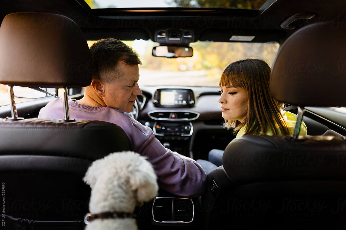 A man and a woman turn to the dog while sitting in the car