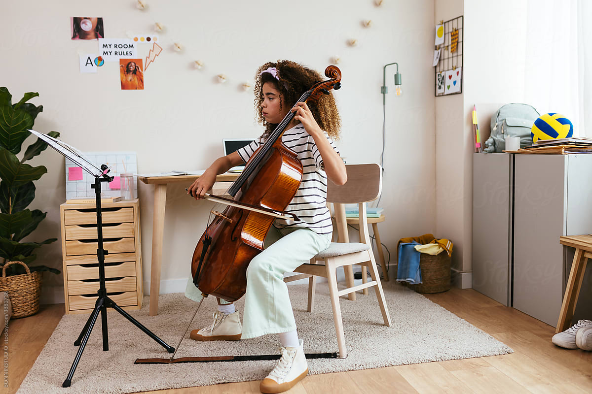 Little music student playing cello at home