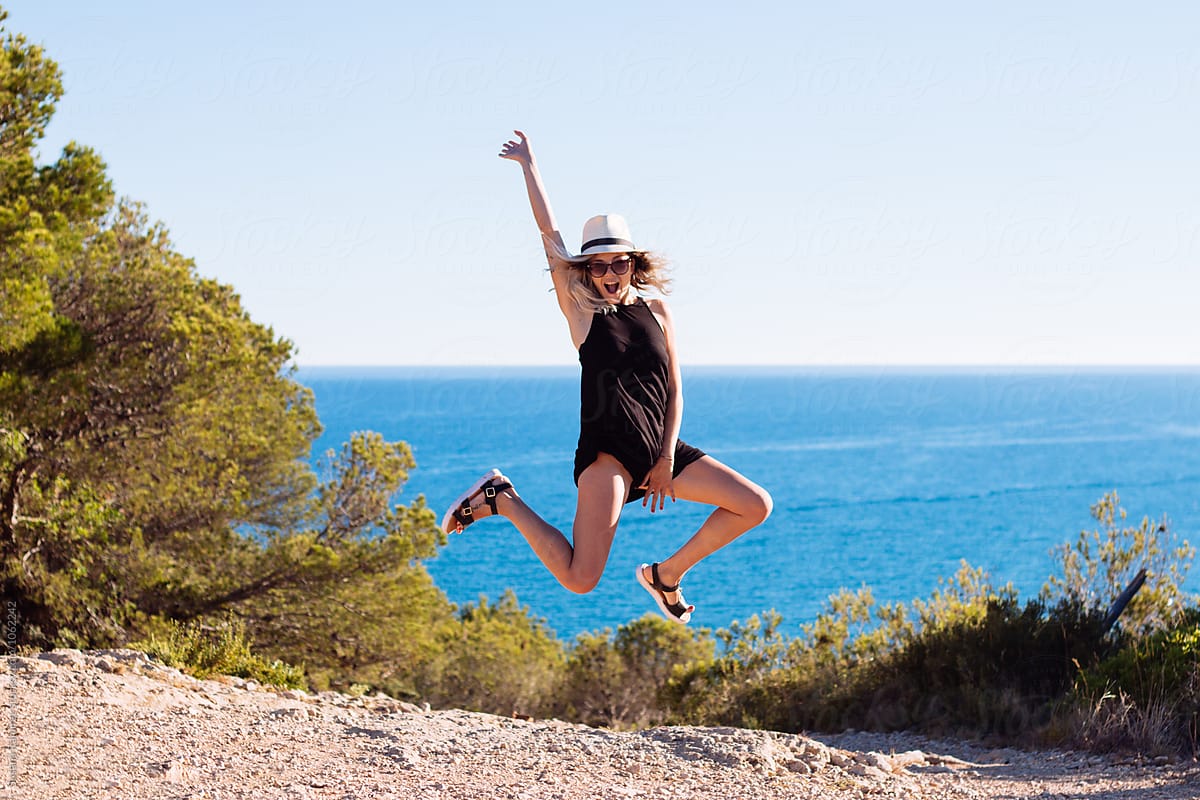 Portrait of young woman jumping on the field, with the sea background