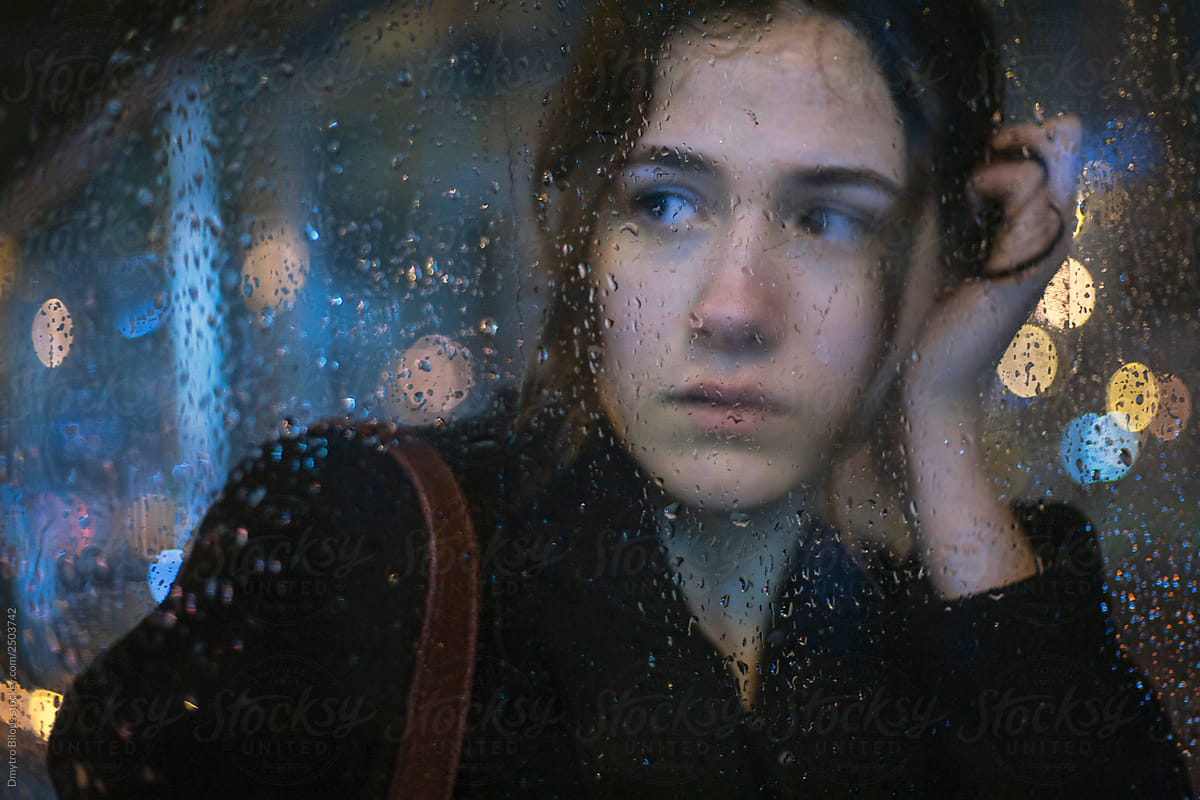 portrait of attractive brunette girl through wet glass during rain