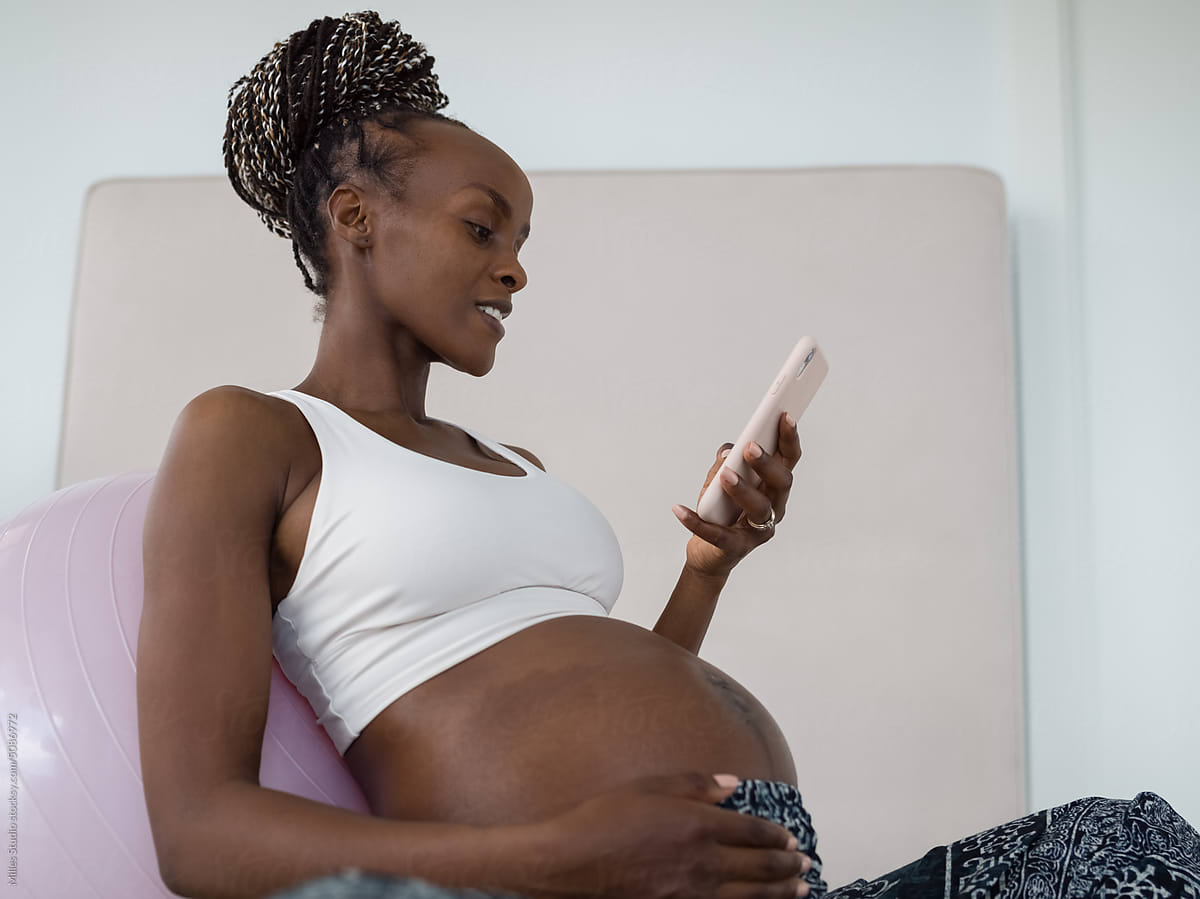 Smiling young future mother using mobile after workout