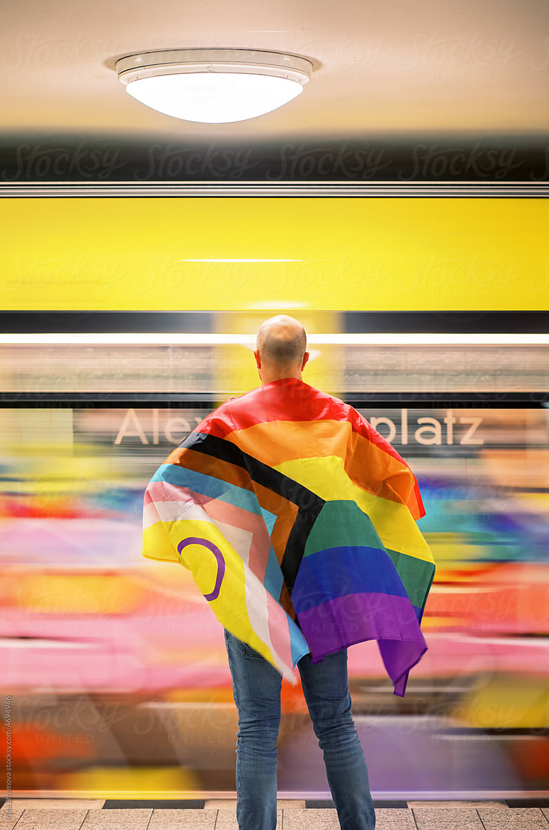 Man wrapped in pride flag in underground waiting for a train