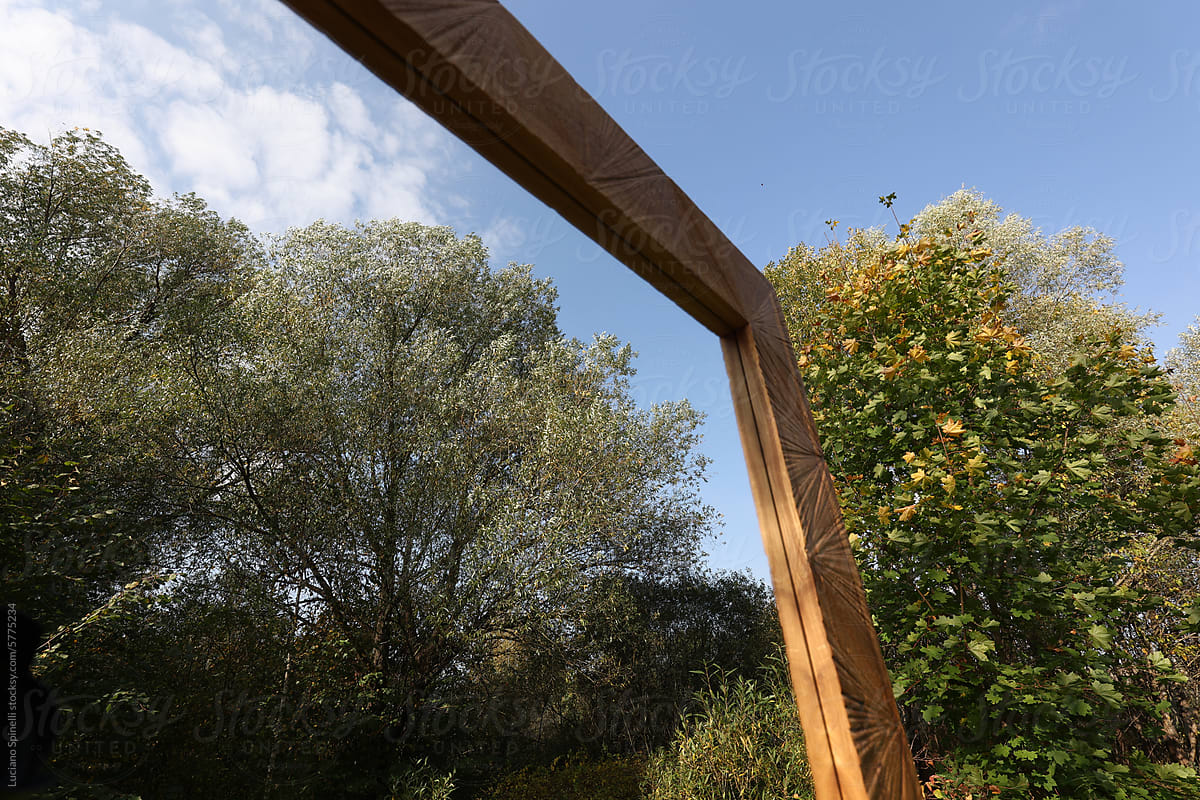Handmade wooden frame mirror reflecting trees and blue sky outdoors