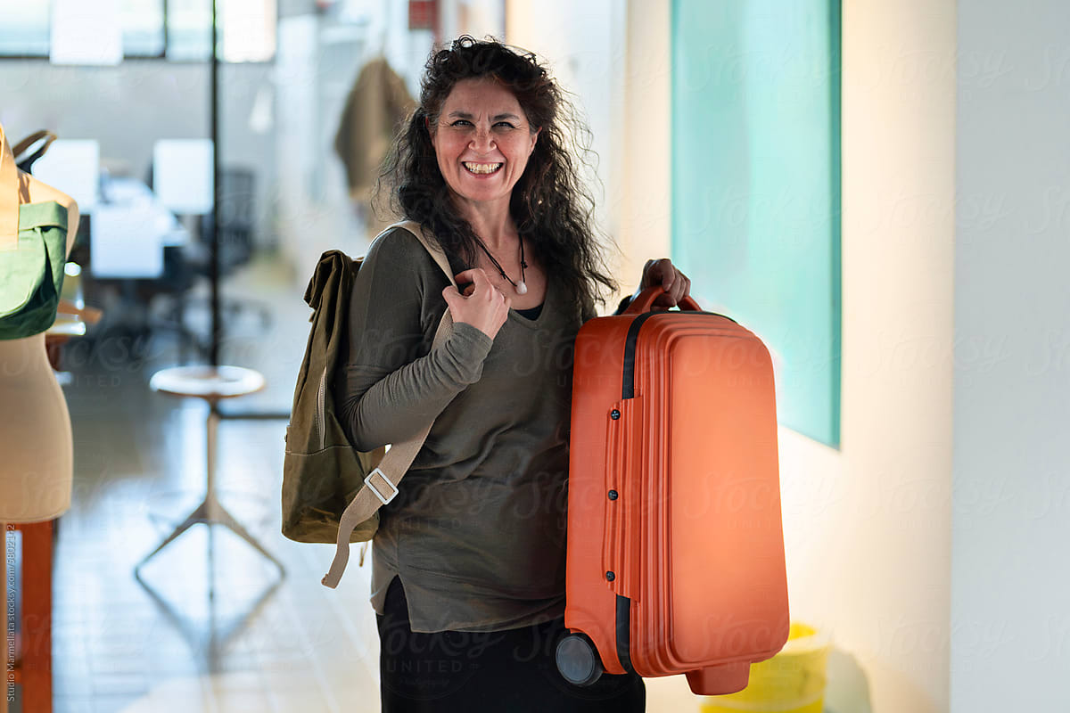 Happy woman standing and showing backpack suitcase in workplace