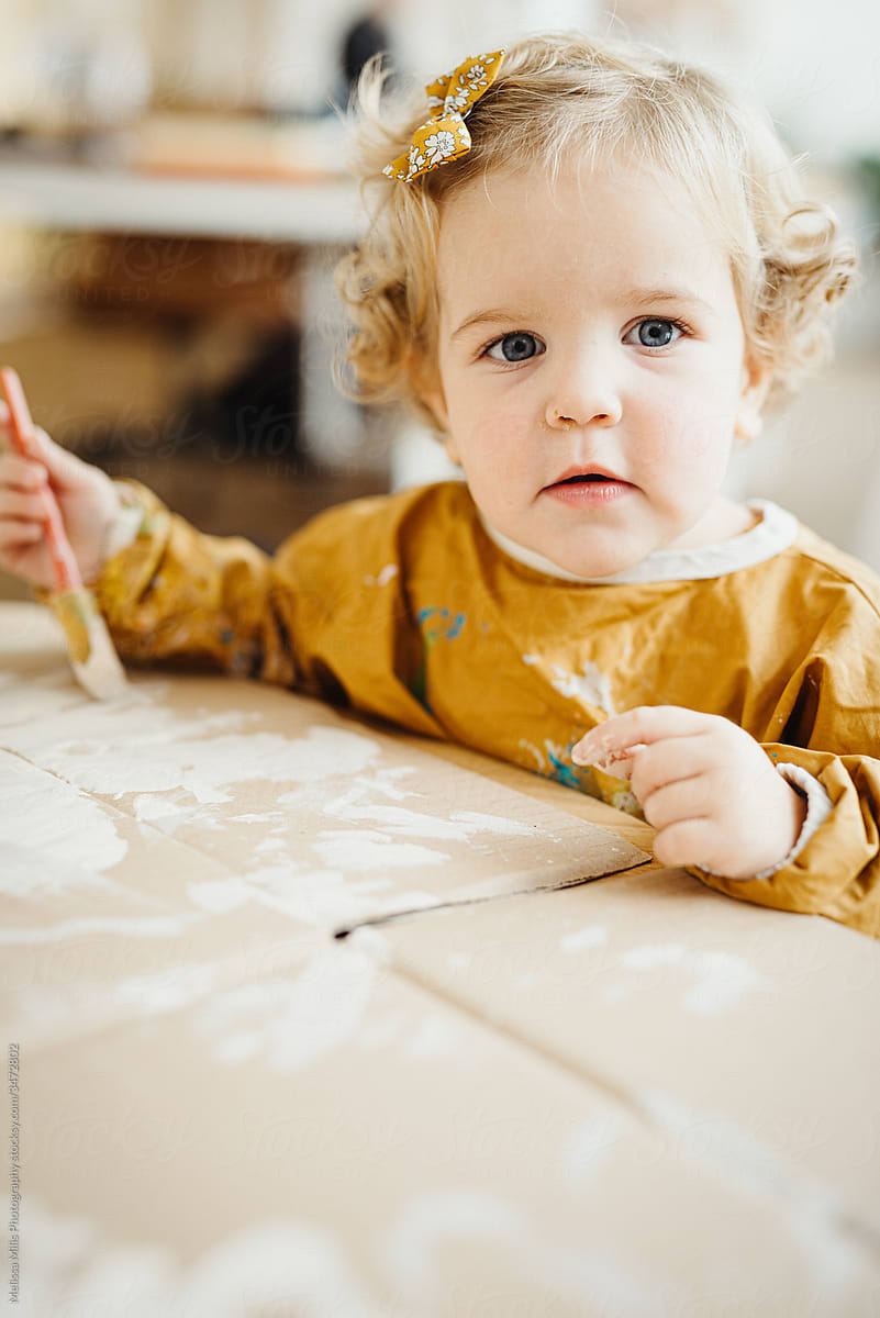 Sweet little blonde girl painting on cardboard