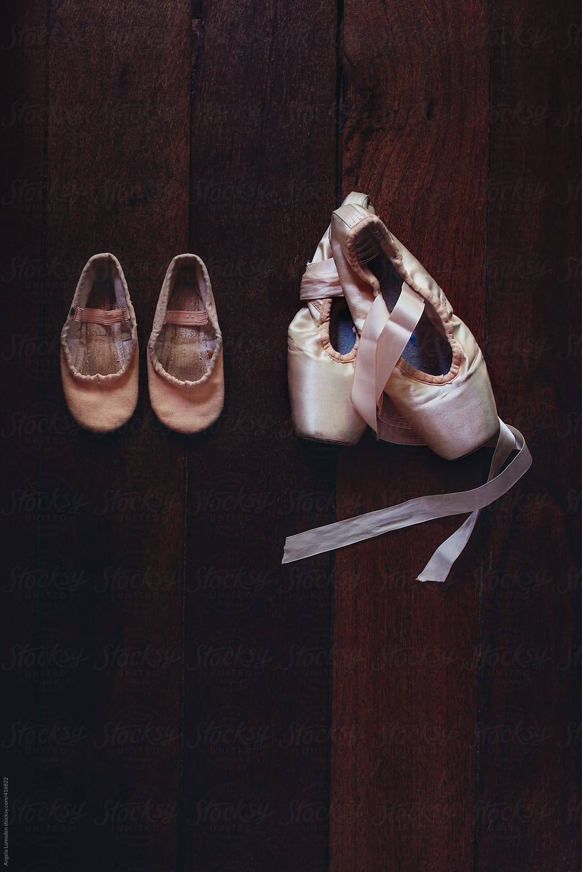 A pair of very small used ballet shoes beside a new pair of pointe shoes