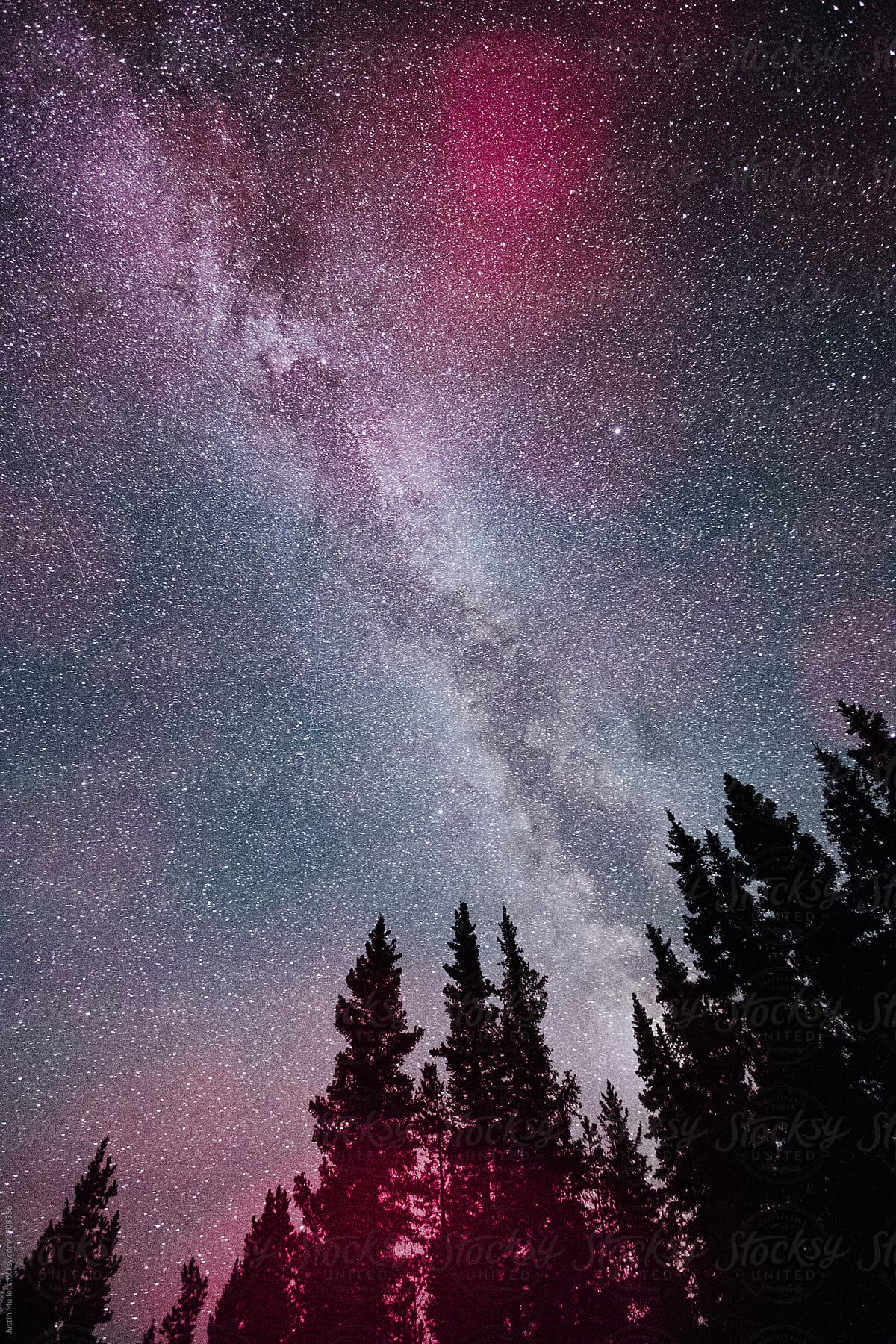 Pink light flares underneath milky way galaxy night sky.
