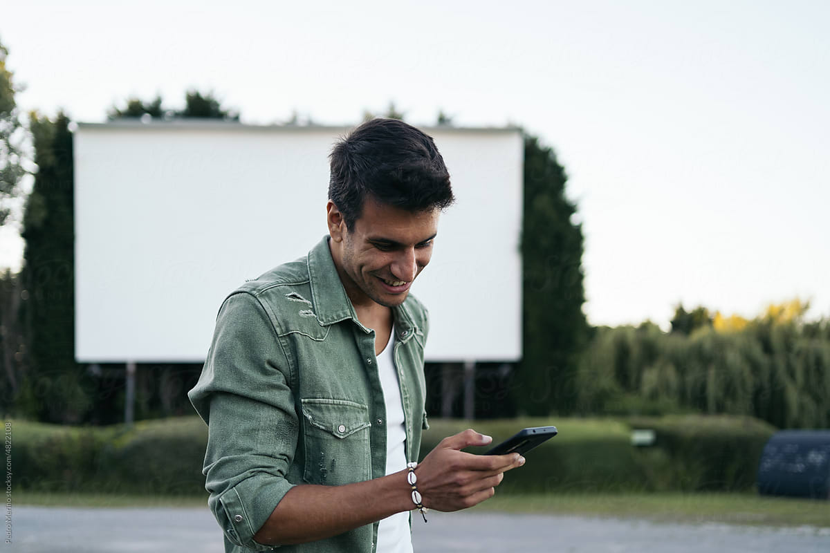 Cheerful man using smartphone at an outdoors drive-in cinema