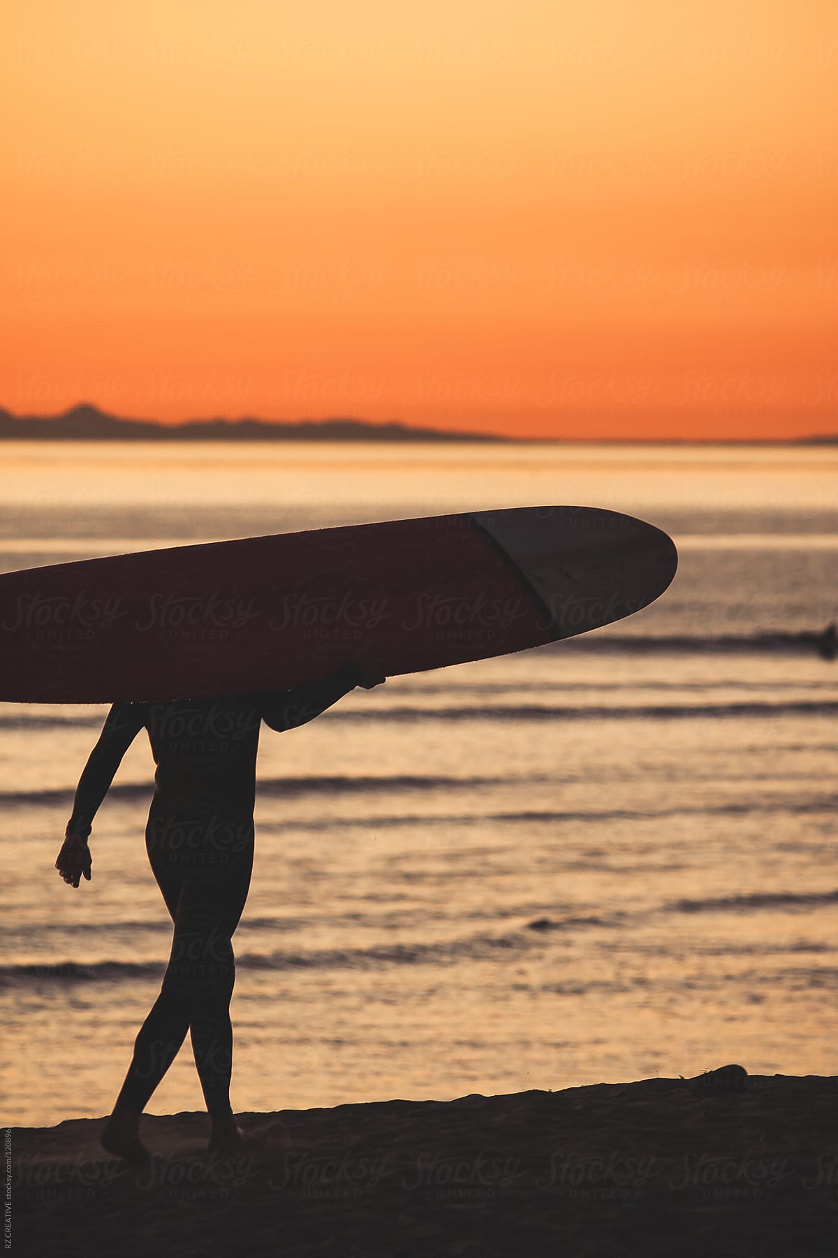 Surfer carrying board at sunset
