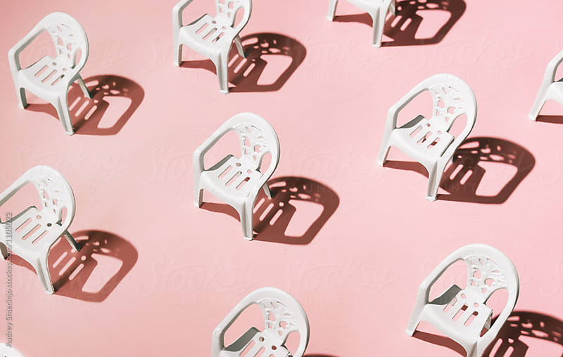 Arranged white chairs in order on pink background.