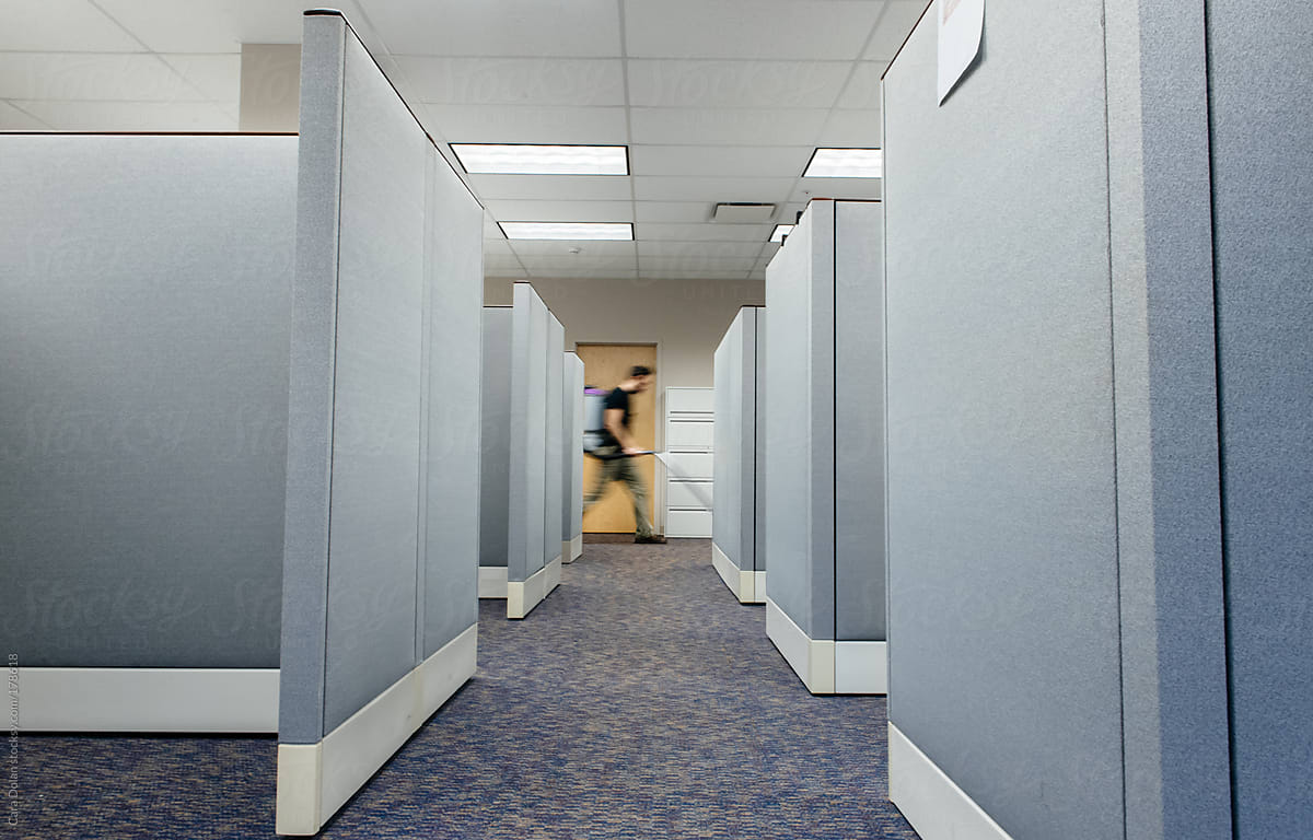 Janitor walks by office cubicle area with vacuum cleaner on his back