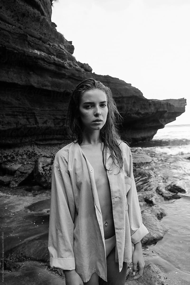 black and white portrait of a girl in a shirt on a naked body on a black sandy beach near the sea