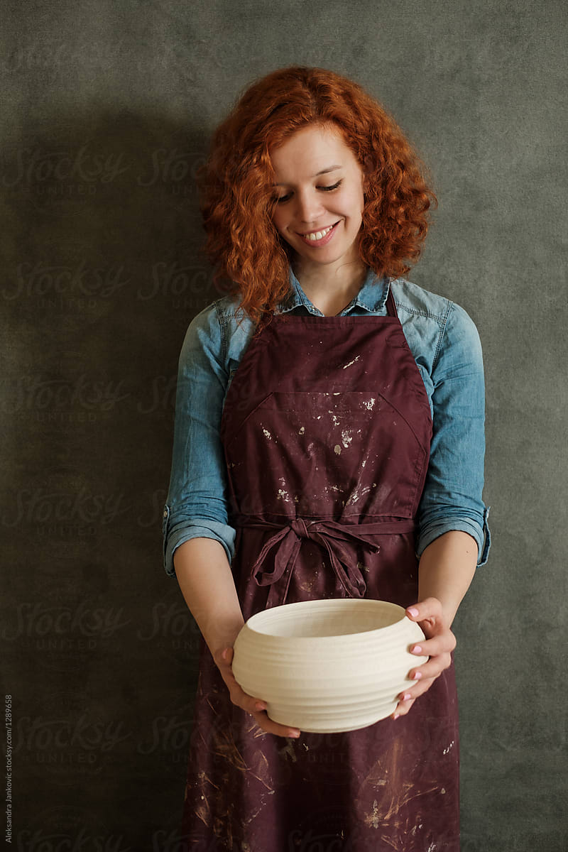 Smiling Female Artisan Holding A Dry Clay Bowl In The Pottery Workshop