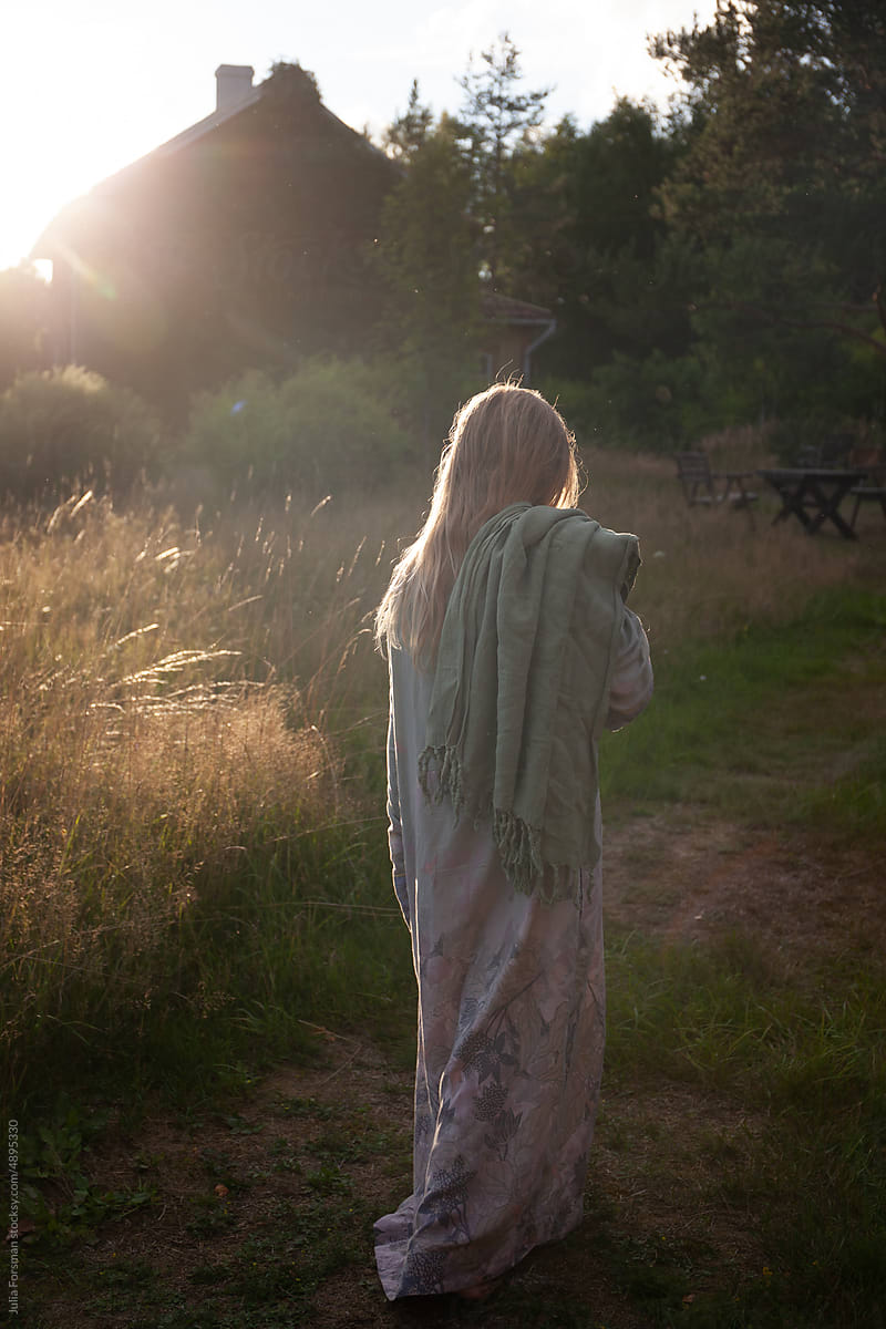 Girl in  a dressing gown carrying  a towel walks in a meadow.