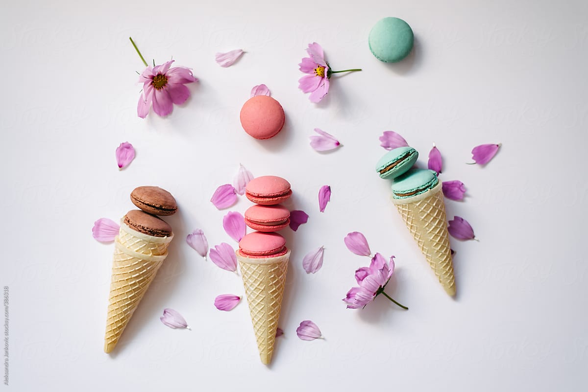Colorful macaroons in cones with pink flowers on white background