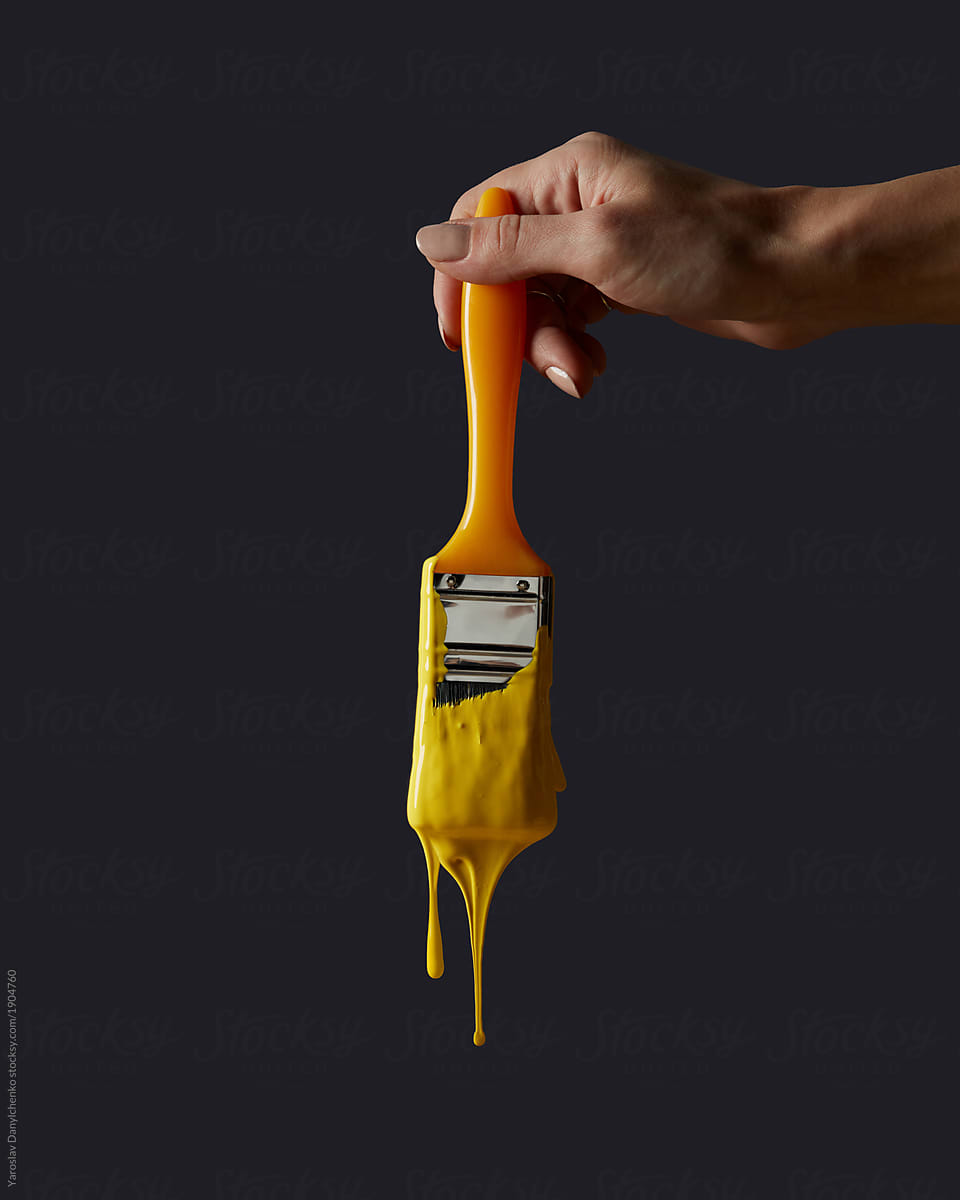 A woman\'s hand holds a brush with yellow paint on a black backgr