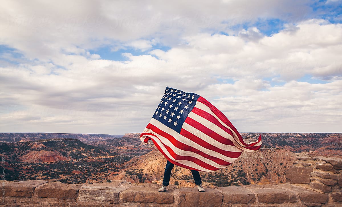 Man Waving An American Flag Overlooking A Canyon