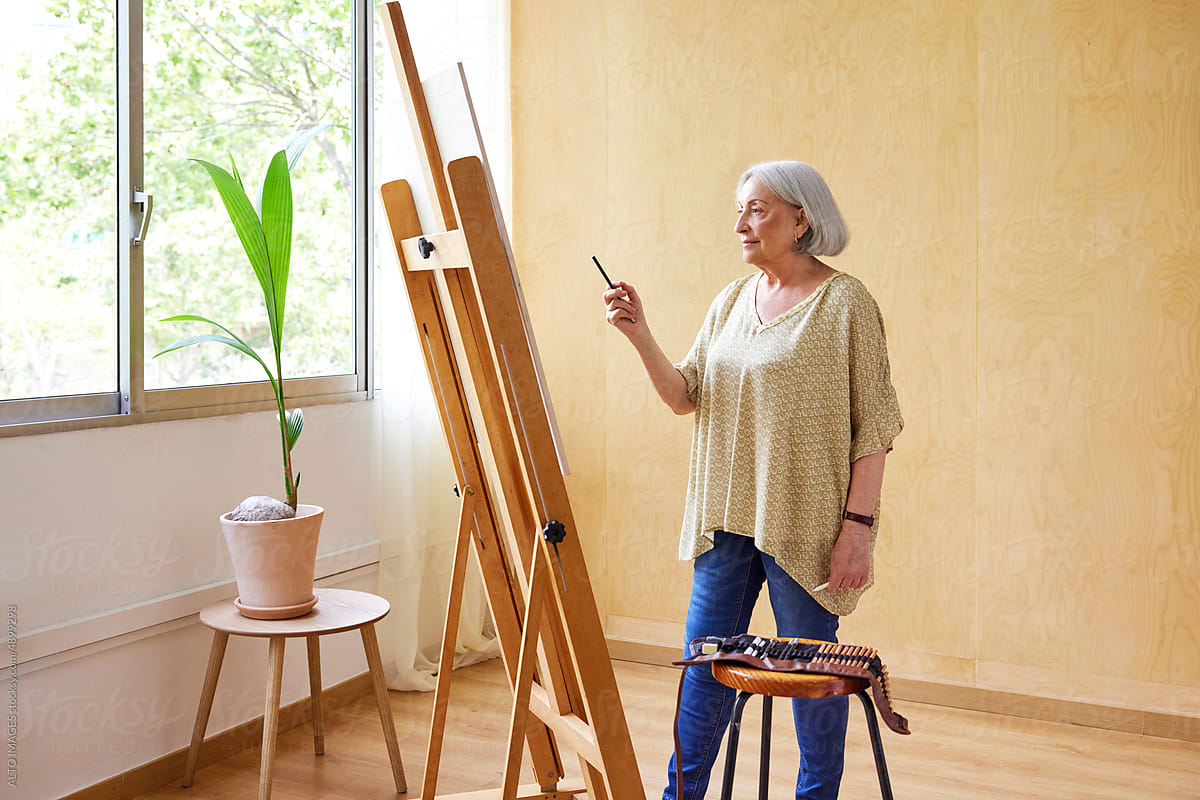 Senior female artist admiring drawing on easel